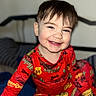 baby, bed, bright_colors, child, clothing_pattern, cute, face, hair, happy, head, home, indoor, pajamas, person, portrait, red_clothing, sitting, smiling, toddler, young_child