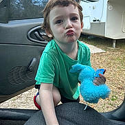 Eli is registered to the contest to win money with this photo: child, toddler, green_shirt, stuffed_toy, blue_toy, pacifier, car_door, car_seat, outdoor, grass, camper, playful, pout, young_child, person, short_hair, daylight, casual, cute, toy