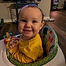 baby, child, infant, smiling, happy, portrait, indoor, living_room, activity_seat, high_chair, yellow_clothing, toy, playtime, television, wood_floor, home, sitting, face, hands, colorful