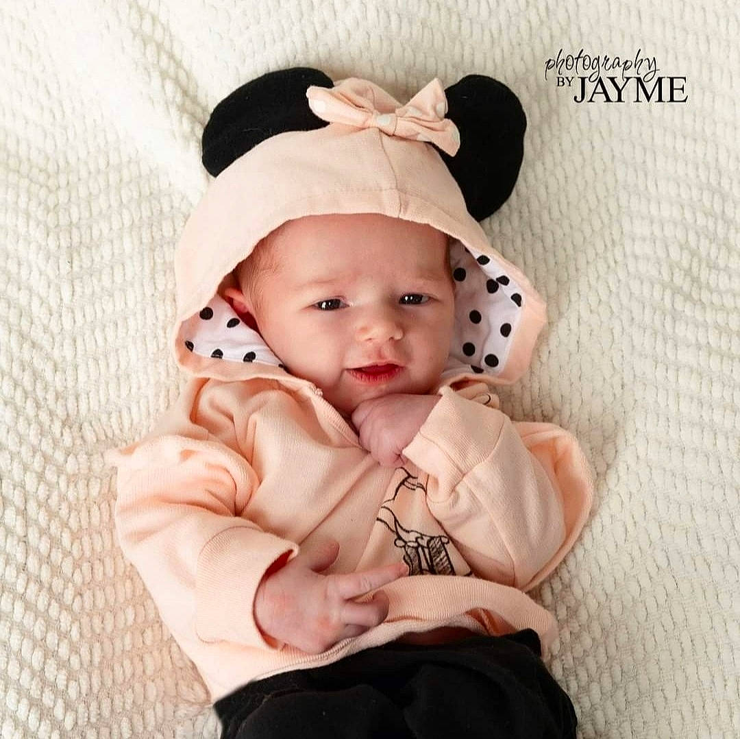 Amirah is registered to the contest to win money with this photo: arm, baby, baby_toddler_clothing, cap, collar, costume_hat, dress, eyelash, face, hand, happy, head, headgear, headwear, human_body, lip, neck, person, pink, product