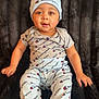 baby, child, infant, clothing, hat, onesie, pants, champion_brand, logo, pattern, sitting, blanket, black_background, cute, portrait, indoors, smiling, face, young, cozy