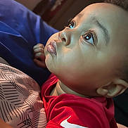 Chakhai joined the competition — help win amazing prizes! baby, child, face, eyes, expression, red_shirt, nike_logo, curly_hair, closeup, portrait, indoor, blanket, pattern, skin, lips, young_child, resting, soft_light, thoughtful, person