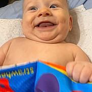 Lucian joined the competition — help win amazing prizes! baby, smiling, child, book, colorful, hand, face, cheeks, bed, blanket, happy, skin, indoors, portrait, infant, expression, cute, young, person, holding