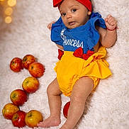 älba participe au concours pour gagner de l'argent avec cette photo : apples, baby, blanket, blue_top, bokeh, child, colorful, cute, fluffy, fruit, indoors, infant, lights, lying_down, portrait, princess_outfit, red_headband, smiling, soft_texture, yellow_bottom