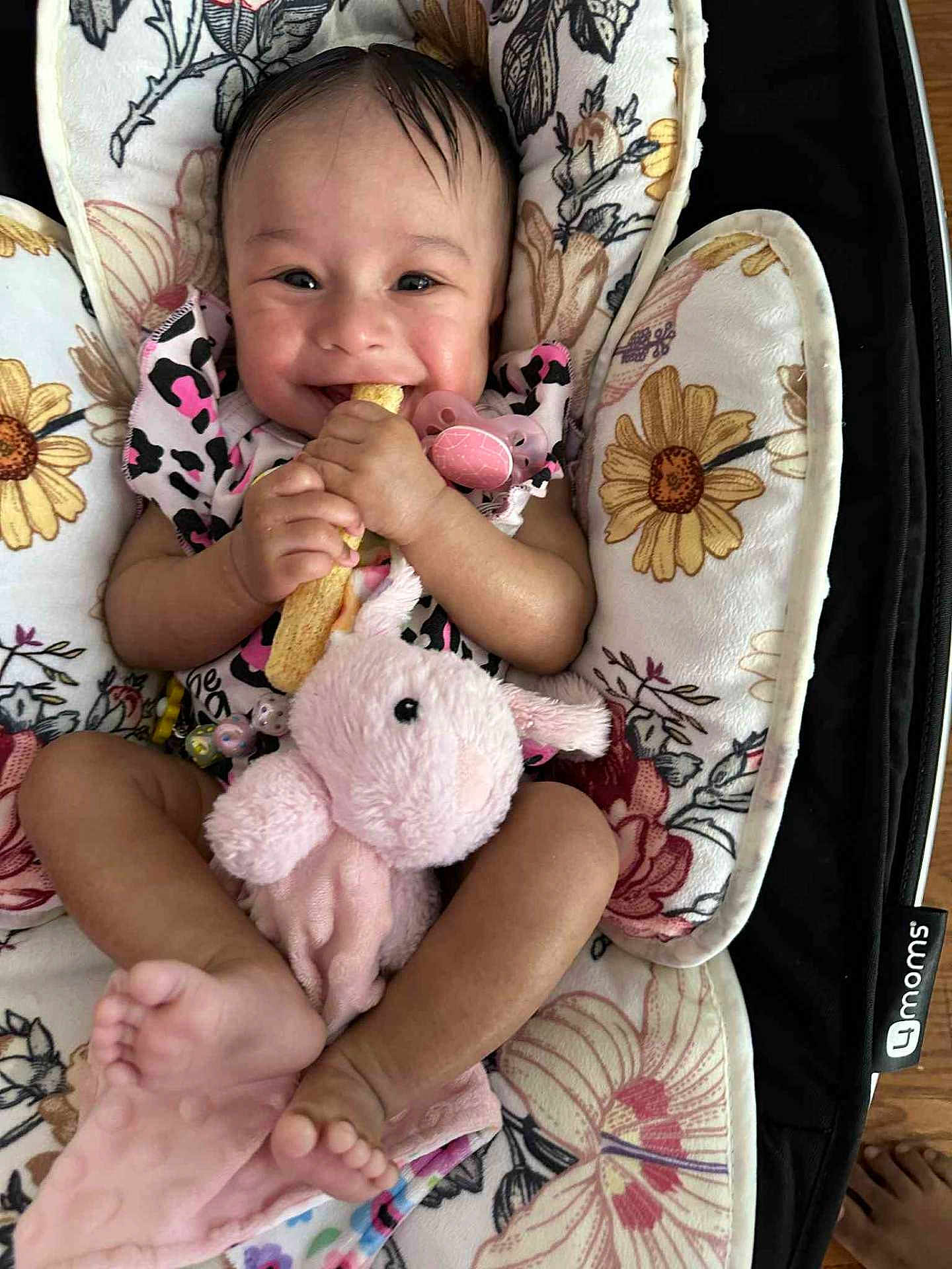 Eliana is registered to the contest to win money with this photo: baby, smiling, infant, pacifier, stuffed_animal, toy, floral_pattern, cushion, seat, barefoot, clothing, hand, foot, face, happy, indoor, person, child, comfort, snack
