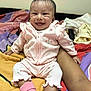 Eliana is registered to the contest to win money with this photo: baby, infant, smiling, pink_outfit, strawberry_print, socks, bedspread, colorful, arm, supporting, happy, cute, portrait, indoors, child, person, young, sitting, clothing, expression