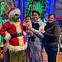 Madison joined the competition — help win amazing prizes! baby, casual_clothing, child, christmas, costume, decorations, family, festive, green_face_paint, grinch, holiday, indoor, lights, person, red_clothing, santa_hat, smile, stone_wall, wood_floor, wreath