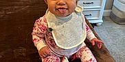 Brielle is registered to the contest to win money with this photo: baby, child, infant, pink_bow, headband, tongue_out, pajamas, bib, white_socks, brown_blanket, smiling, curly_hair, indoor, carpet, dresser, lamp, pacifier_clip, cute, happy, portrait