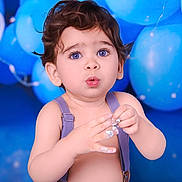 Diego is registered to the contest to win money with this photo: baby, balloons, blue_background, blue_eyes, celebration, child, closeup, cream, curly_hair, cute, expression, fun, hands, indoor, person, portrait, skin, surprised, suspenders, toddler
