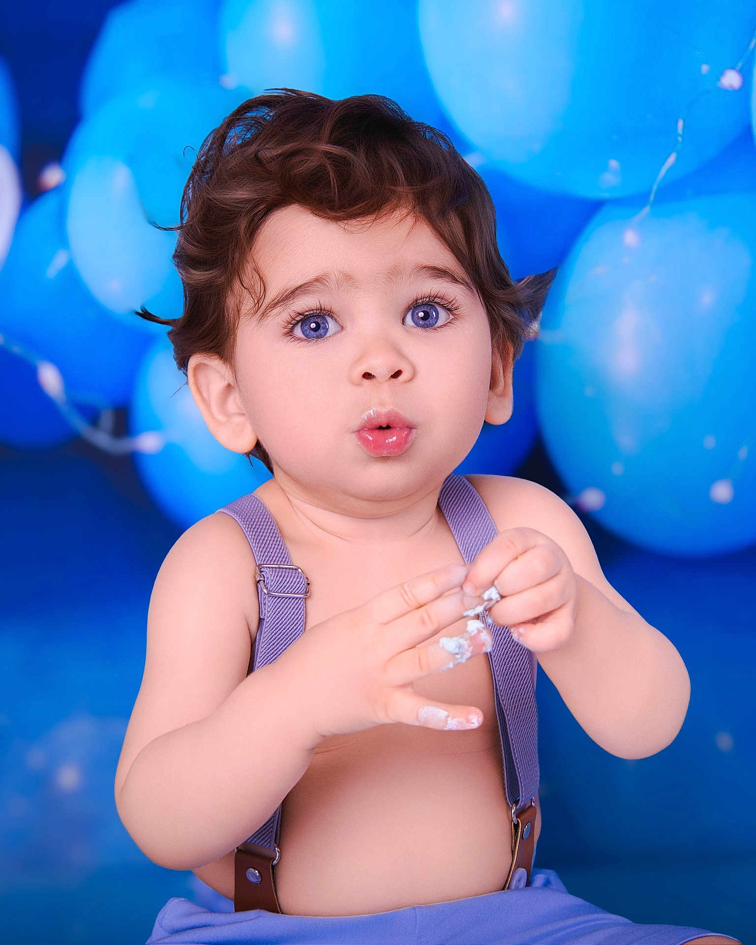 Diego is registered to the contest to win money with this photo: baby, balloons, blue_background, blue_eyes, celebration, child, closeup, cream, curly_hair, cute, expression, fun, hands, indoor, person, portrait, skin, surprised, suspenders, toddler