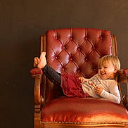 Ayana participe au concours pour gagner de l'argent avec cette photo : child, toddler, smiling, chair, red_leather, armchair, legs_up, long_sleeve_shirt, skirt, indoor, wooden_armrests, happy, blond_hair, casual_clothing, relaxed, furniture, portrait, cute, person, home