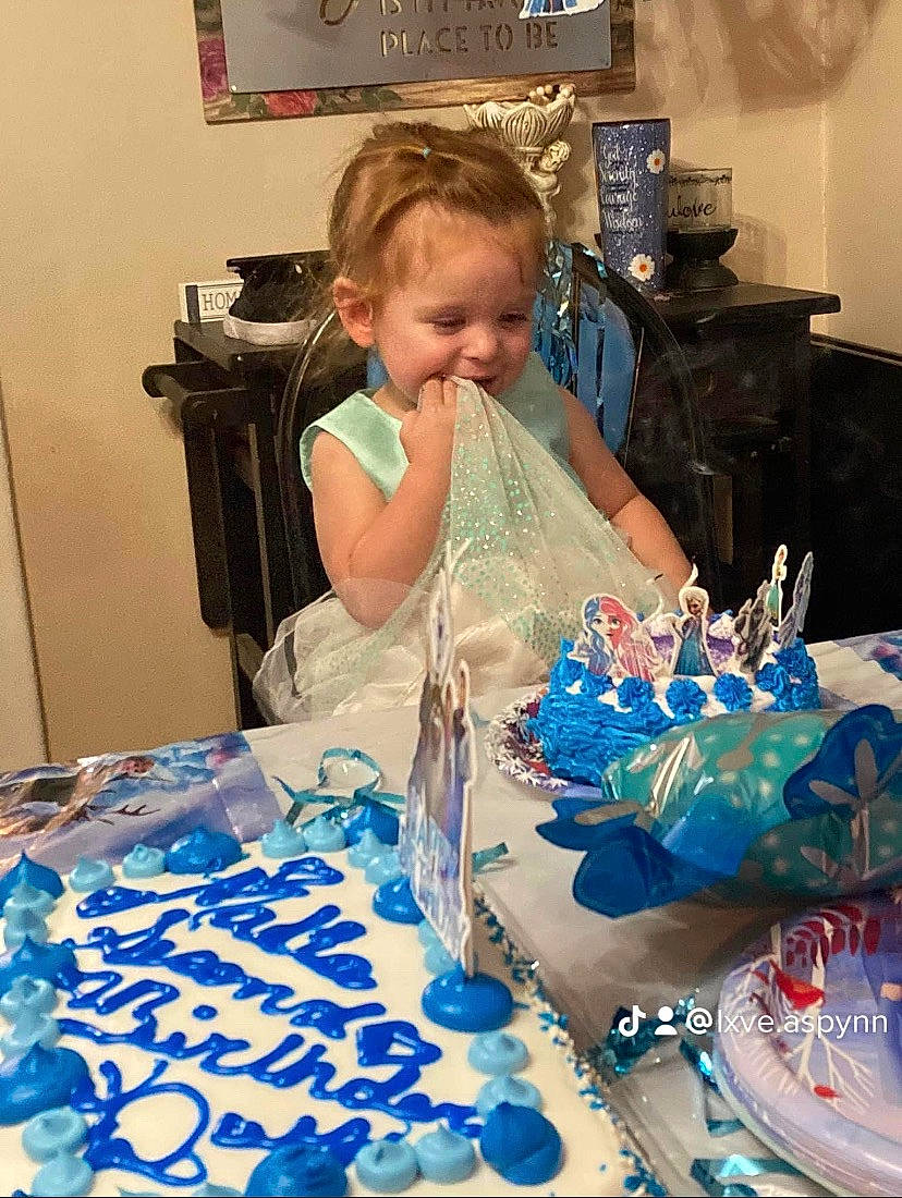 Malia is registered to the contest to win money with this photo: baby_toddler_clothing, baked_goods, birthday, blue, buttercream, cake, cake_decorating, cake_decorating_supply, child, electric_blue, event, food, fun, happy, person, picture_frame, sugar_cake, table, television, textile