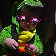 Bryden is registered to the contest to win money with this photo: child, costume, dinosaur, glasses, toy, candy, stroller, green, yellow, pink, baby, cute, funny, hand, face, clothing, indoor, portrait, infant, playful