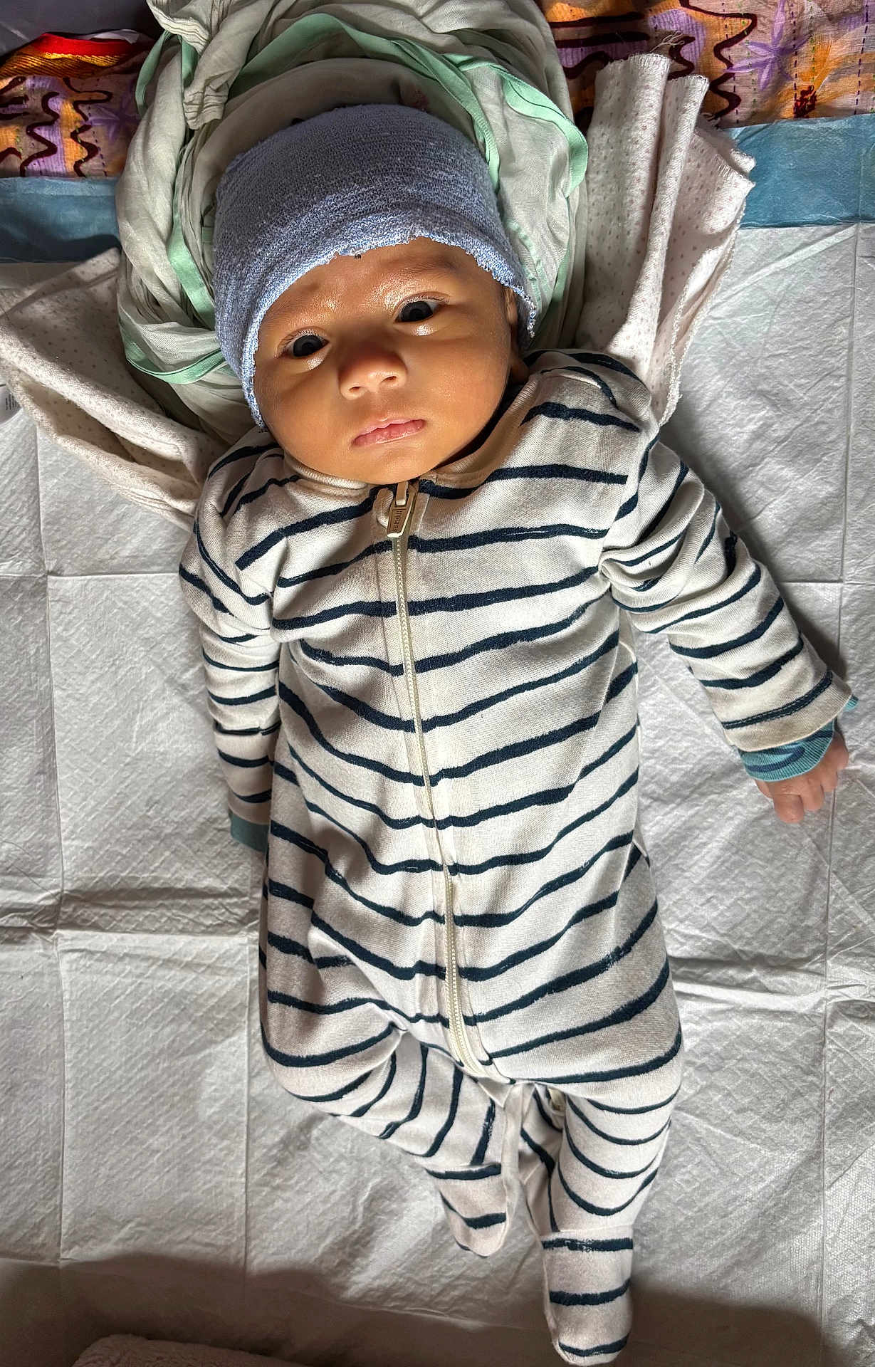 Arita joined the competition — help win amazing prizes! baby, infant, striped_clothing, onesie, hat, blanket, fabric, lying_down, face, newborn, child, soft_lighting, indoors, sleepwear, portrait, cute, small_hands, head_covering, curious_expression, baby_gaze