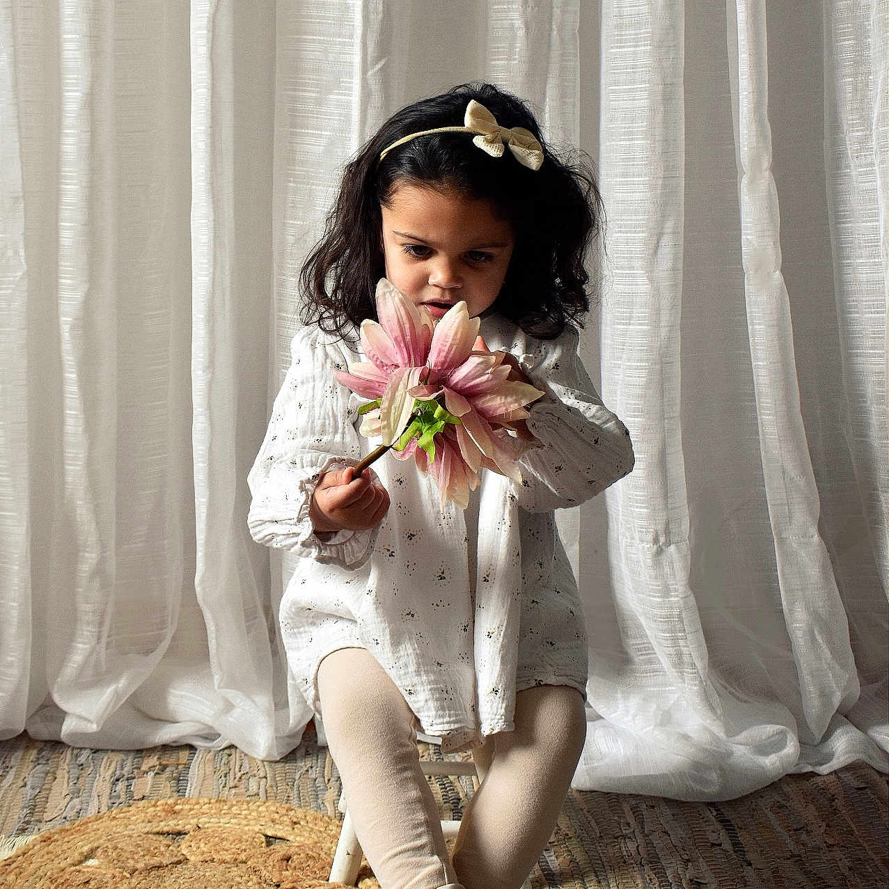 Mya a rejoint le concours — aidez-le/la à gagner de superbes lots ! barefoot, chair, child, crossed_legs, curly_hair, curtains, cute, decor, flower, girl, headband, home, indoors, looking_down, playful, rug, small, soft_light, white_dress, young