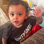 Jack joined the competition — help win amazing prizes! toddler, child, curly_hair, indoor, couch, toys, hand, face, clothing, curious, young_child, home, colorful, expression, person, brown_eyes, black_shirt, wooden_floor, background, furniture