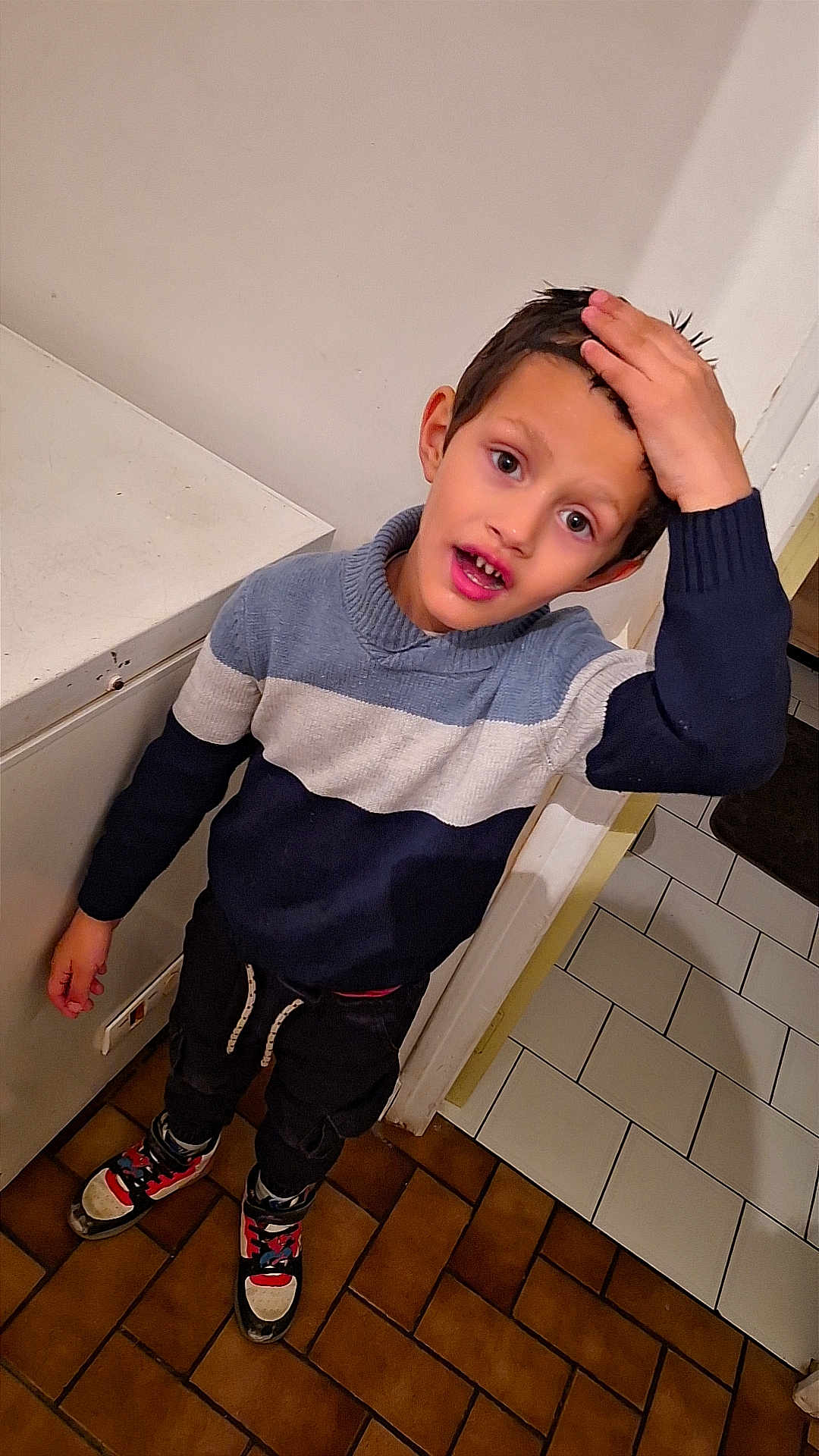 Gabriel participe au concours pour gagner de l'argent avec cette photo : child, boy, indoor, sweater, sneakers, tiled_floor, hand_on_head, curious_expression, standing, person, young, clothing, floor, doorway, wall, casual, portrait, looking_up, short_hair, home