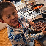 Suan participe au concours pour gagner de l'argent avec cette photo : appliance, boy, casual, child, chocolate, closed_eyes, cooking, countertop, cupboard, funny_face, kitchen, pajamas, pan, sink, smiling, stirring, stool, tiles, utensils, wood_floor
