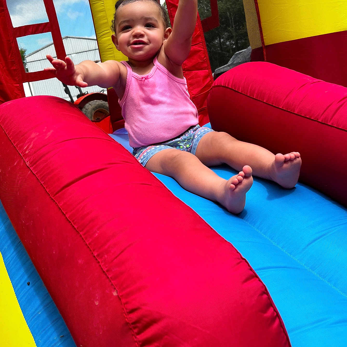 Railee is registered to the contest to win money with this photo: arms_up, barefoot, blue, child, daytime, excited, fun, happy, inflatable_slide, outdoor, pink_tank_top, play, recreation, red, shorts, smiling, summer, sunny, toddler, yellow