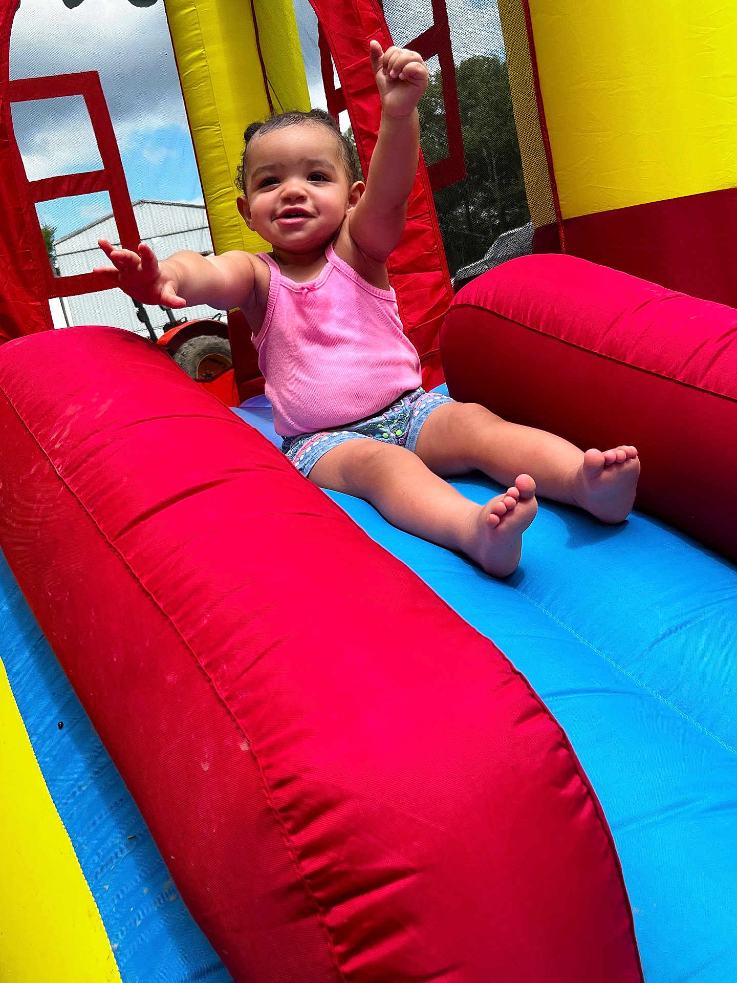 Railee is registered to the contest to win money with this photo: toddler, child, smiling, pink_tank_top, shorts, inflatable_slide, red, yellow, blue, outdoor, sunny, fun, play, happy, arms_up, barefoot, summer, daytime, excited, recreation