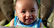 Riley is registered to the contest to win money with this photo: baby, blue, cheerful, child, clothing, curly_hair, cute, expression, face, happy, head, high_chair, indoor, infant, person, portrait, seat, skin, smiling, young