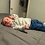 baby, bed, blanket, blue_jeans, clothing, cute, face, furniture, indoor, infant, jeans, lying_down, person, portrait, room, sleeve, socks, striped_sweater, toddler, young_child