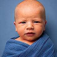 Justin is registered to the contest to win money with this photo: baby, infant, portrait, blue_blanket, wrapped, serious_expression, closeup, head, face, skin, newborn, soft_texture, studio, indoor, person, cute, young_child, warm, babywearing, blue_background