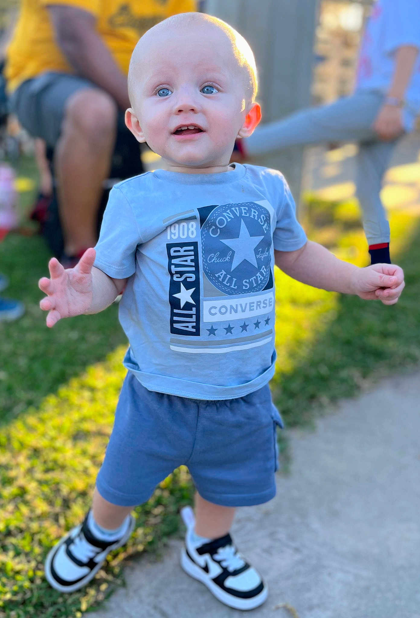 Ryder is registered to the contest to win money with this photo: toddler, child, boy, standing, outdoor, sunlight, blue_eyes, shorts, tshirt, sneakers, grass, sidewalk, smile, happy, converse, person, casual_clothing, daylight, blurred_background, playful