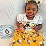 baby, infant, child, smiling, tongue_out, bee_pattern, yellow_skirt, white_shirt, hair_bows, cute, playful, sitting, blanket, sign, 6_months, portrait, closeup, happy, indoors, person