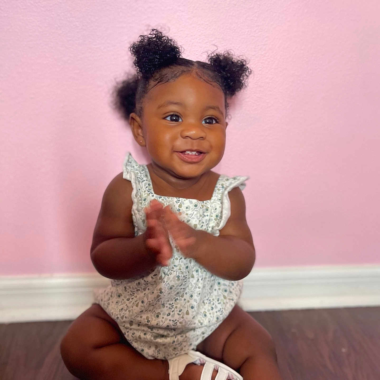 Layla is registered to the contest to win money with this photo: baby, child, clapping, curly_hair, cute, floor, footwear, happy, indoors, infant, person, pigtails, pink_wall, portrait, sitting, skin, smiling, white_dress, white_sandals, wooden_floor