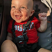 Cooper is registered to the contest to win money with this photo: baby, child, smiling, happy, face, red_shirt, stroller, safety_strap, sunlight, dimples, skin, hand, foot, infant, cute, portrait, closeup, daylight, person, outdoor