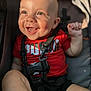 baby, child, smiling, happy, face, red_shirt, stroller, safety_strap, sunlight, dimples, skin, hand, foot, infant, cute, portrait, closeup, daylight, person, outdoor