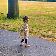 Airah is registered to the contest to win money with this photo: child, park, coat, dinosaur_pattern, butterfly_pattern, boots, paved_path, grass, tree, outdoor, nature, curious, young_child, casual_clothing, walking, daylight, fall, scenery, person, portrait