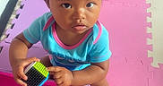 Ellayah joined the competition — help win amazing prizes! toddler, child, curly_hair, toy, block, colorful, play_mat, pink, purple, blue_shirt, indoor, looking_up, person, cute, baby, hands, sitting, floor, expression, young_child