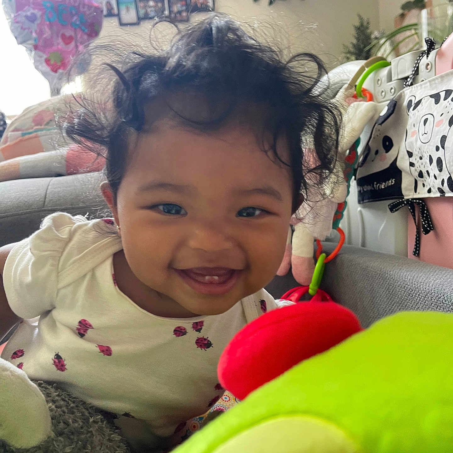 Ellayah is registered to the contest to win money with this photo: baby, smiling, curly_hair, indoor, toy, plush_toy, living_room, plant, family_photos, couch, child, cute, happy, person, clothing, infant, colorful, playful, portrait, home