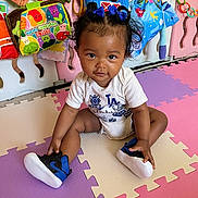 Ellayah joined the competition — help win amazing prizes! baby, child, sitting, play_mat, colorful, onesie, sneakers, blue_bows, curly_hair, toys, educational_toys, indoor, play_area, smiling, person, infant, cute, floor, happy, home