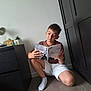 boy, child, reading, book, indoor, floor, furniture, cabinet, sock, shorts, tshirt, concentration, portrait, home, casual, young, brown_hair, light, shadow, relaxation