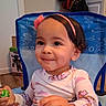 toddler, child, smile, face, headband, flower, toy, chair, indoor, clothing, long_sleeve, patterned_clothing, hair, cute, person, young_child, furniture, background, happy, seated