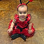baby, child, costume, ladybug, red_dress, headband, antennae, smile, happy, sitting, floor, wooden_floor, cute, indoors, person, black_shoes, toddler, playful, portrait, fun