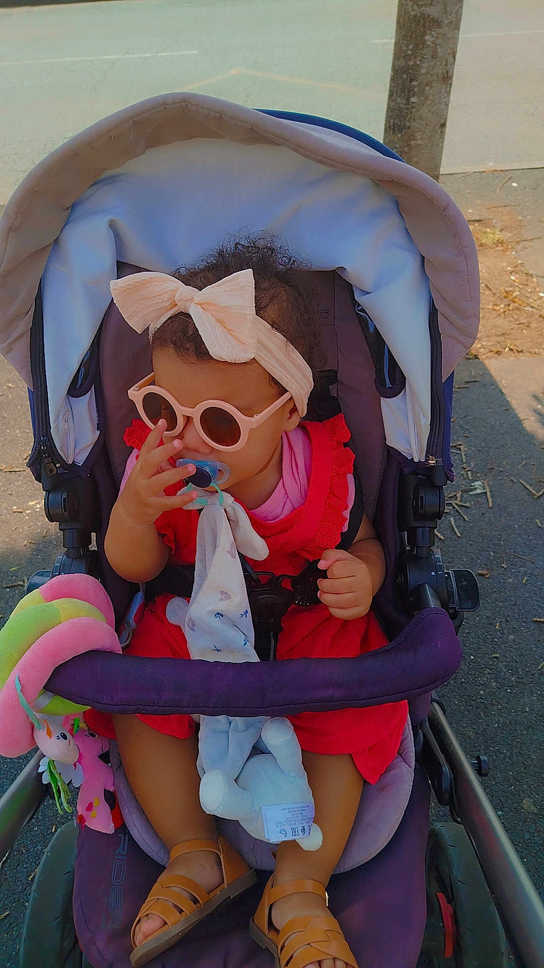 Orabella a rejoint le concours — aidez-le/la à gagner de superbes lots ! toddler, stroller, sunglasses, headband, pacifier, toy, outdoor, child, footwear, red_dress, baby, sunlight, seat, cute, accessory, summer, person, walking, shade, sidewalk