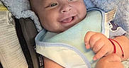Elias is registered to the contest to win money with this photo: baby, smiling, bib, bottle, blanket, infant, happy, cute, chubby_cheeks, face, person, indoor, closeup, newborn, child, soft_lighting, comfort, car_seat, red_bracelet, cozy