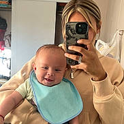 Elias is registered to the contest to win money with this photo: baby, bib, person, mirror, phone, selfie, smile, indoor, clothing, hand, hair, hoodie, shorts, room, door, reflection, carpet, casual, holding, portrait