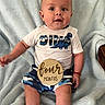 Elias is registered to the contest to win money with this photo: baby, infant, child, dinosaur, plaque, milestone, four_months, clothing, shorts, tshirt, socks, blanket, soft_texture, cute, portrait, sitting, indoors, happy, person, young_child