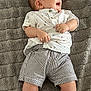 baby, blanket, casual_clothing, child, cute, face, happy, head, indoor, infant, lying_down, patterned_clothing, portrait, shirt, shorts, skin, smiling, striped_clothing, textured_blanket, young_child