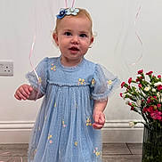 Agnes is registered to the contest to win money with this photo: toddler, child, blue_dress, balloons, flowers, vase, wooden_floor, indoor, smiling, cute, portrait, person, celebration, decor, happy, flower_bow, socks, curly_hair, standing, young_child