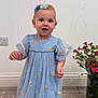 toddler, child, blue_dress, balloons, flowers, vase, wooden_floor, indoor, smiling, cute, portrait, person, celebration, decor, happy, flower_bow, socks, curly_hair, standing, young_child