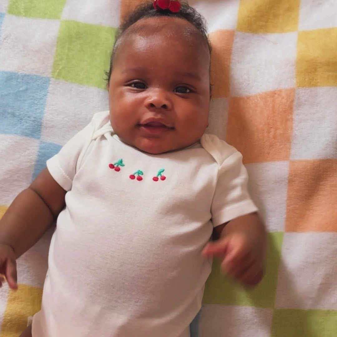 Nyori is registered to the contest to win money with this photo: baby, infant, child, onesie, blanket, cherry, hair_accessory, smiling, lying_down, cute, happy, indoor, portrait, young_child, skin, face, head, clothing, colorful, pattern