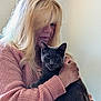 woman, cat, gray_cat, indoor, portrait, holding, pink_sweater, long_hair, blonde_hair, pet, animal, cozy, affection, face, hand, tattoo, calm, closeup, casual, home