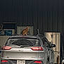 car, cat, container, curious, domestic_animal, dusty, garage, household_items, indoor, jeep, license_plate, metal_wall, orange_cat, pet, rear_view, refrigerator, roof, sitting, storage, vehicle