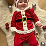 baby, infant, santa_costume, christmas, ornaments, fluffy_rug, dog_peek, holiday, festive, red_outfit, white_trim, belt, smile, portrait, indoor, wooden_floor, cute, celebration, props, hands